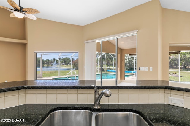 kitchen with a sink, ceiling fan, and dark stone countertops