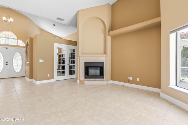 unfurnished living room with visible vents, high vaulted ceiling, a notable chandelier, french doors, and a tile fireplace