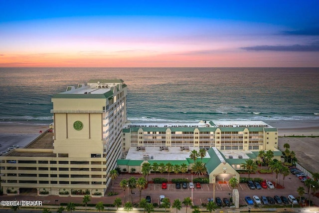 aerial view at dusk featuring a view of the beach and a water view