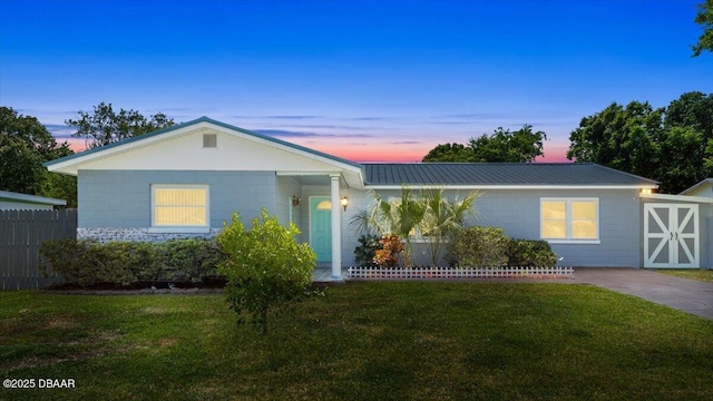 ranch-style house with a yard, fence, metal roof, and concrete block siding