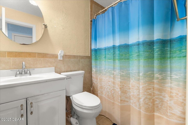 full bath with tile walls, toilet, vanity, curtained shower, and a textured wall