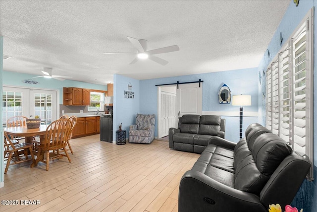 living room featuring light wood-type flooring, a textured ceiling, a barn door, and a ceiling fan
