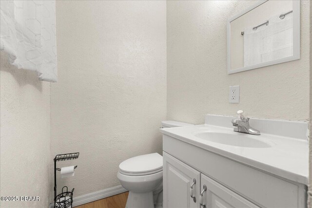 bathroom featuring toilet, baseboards, wood finished floors, and vanity