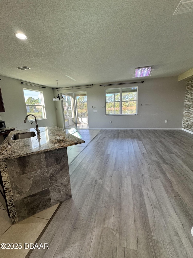 kitchen with light stone countertops, a textured ceiling, sink, light hardwood / wood-style flooring, and a center island with sink