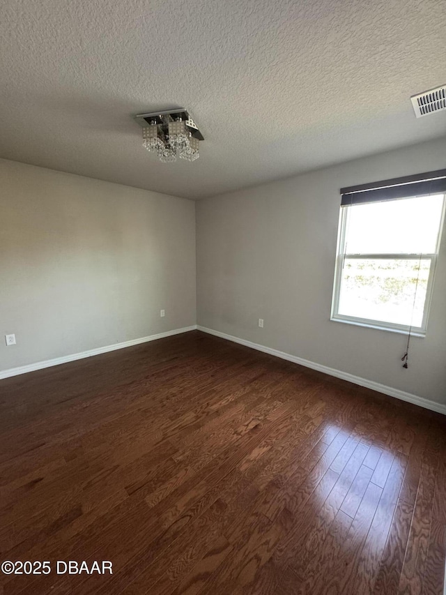 spare room featuring dark wood-style floors, visible vents, a textured ceiling, and baseboards