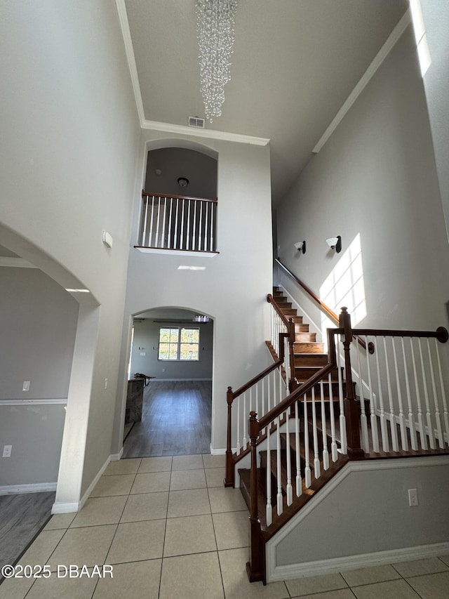 staircase with tile patterned flooring, a towering ceiling, crown molding, and a chandelier