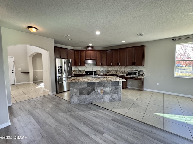 kitchen featuring light stone counters, backsplash, a sink, under cabinet range hood, and stainless steel fridge with ice dispenser