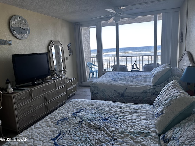 bedroom with a textured ceiling, tile patterned floors, access to exterior, a water view, and ceiling fan