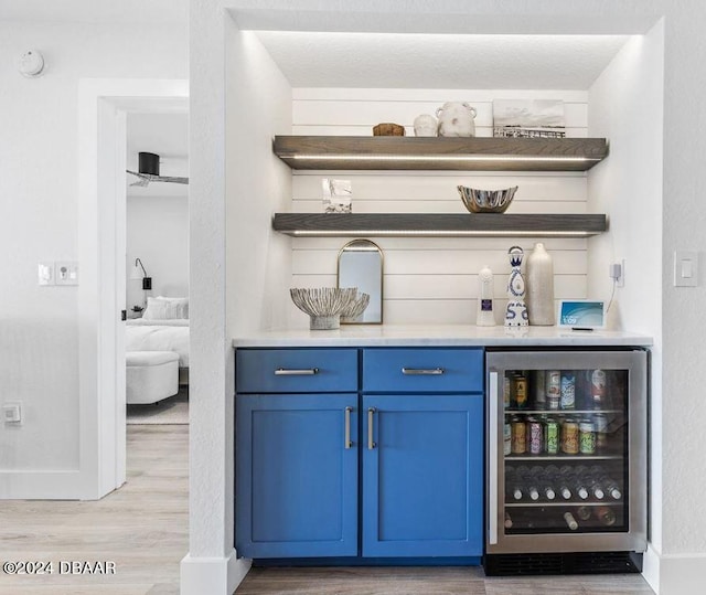 bar featuring blue cabinetry, light hardwood / wood-style flooring, beverage cooler, and stainless steel refrigerator