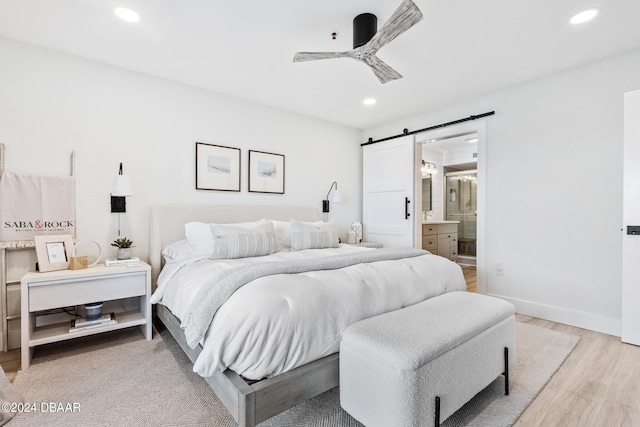 bedroom featuring ensuite bath, a barn door, ceiling fan, and light hardwood / wood-style flooring