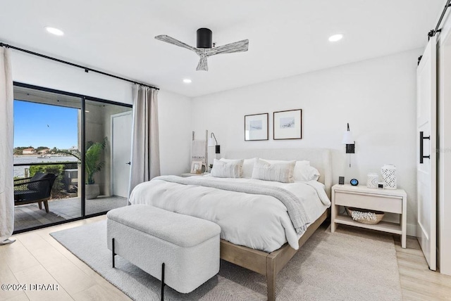 bedroom with light wood-type flooring, a barn door, ceiling fan, and access to exterior