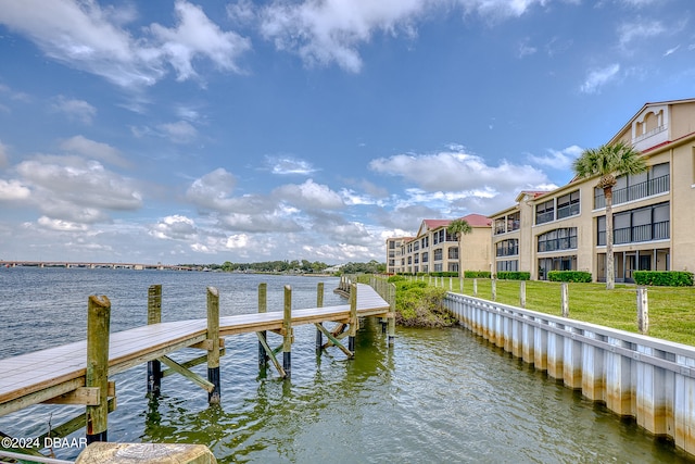 view of dock with a water view, a lawn, and a balcony