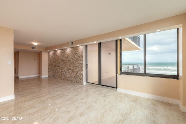 spare room with a water view, a view of the beach, and light wood-type flooring