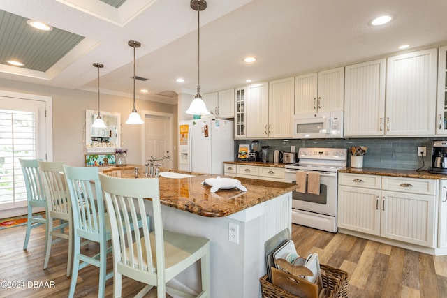 kitchen with dark stone counters, white appliances, a center island with sink, and sink