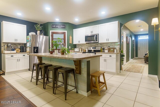 2756 Star Coral Ln, New Smyrna Beach, FL 32168 - kitchen featuring stainless steel appliances, tasteful backsplash, arched walkways, a kitchen breakfast bar, and an island with sink