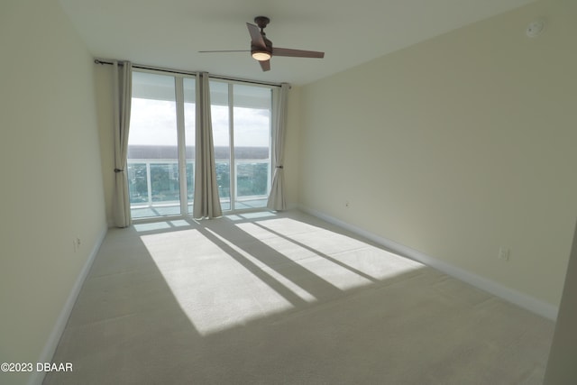 carpeted spare room featuring a water view, a wall of windows, and ceiling fan