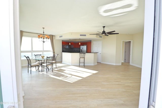 kitchen with light hardwood / wood-style floors, appliances with stainless steel finishes, a kitchen bar, ceiling fan with notable chandelier, and backsplash