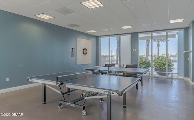 recreation room with a wall of windows, a paneled ceiling, and baseboards