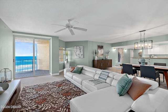 carpeted living room with a textured ceiling, ceiling fan with notable chandelier, and a water view