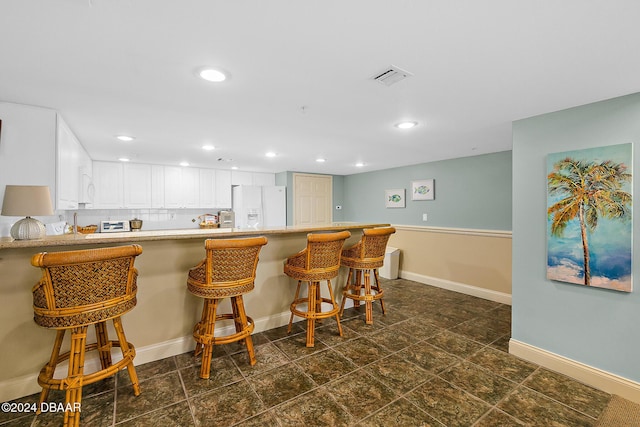 kitchen with kitchen peninsula, white cabinetry, white fridge with ice dispenser, and a breakfast bar area