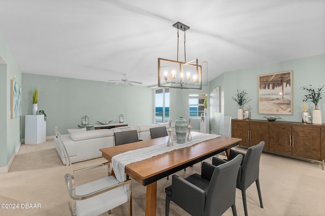 carpeted dining space featuring ceiling fan with notable chandelier and a water view