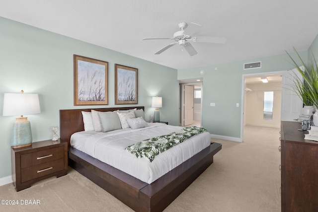 bedroom with ceiling fan, light colored carpet, and ensuite bathroom