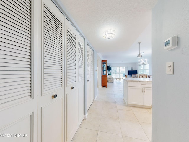 corridor with a notable chandelier, a textured ceiling, and light tile patterned floors