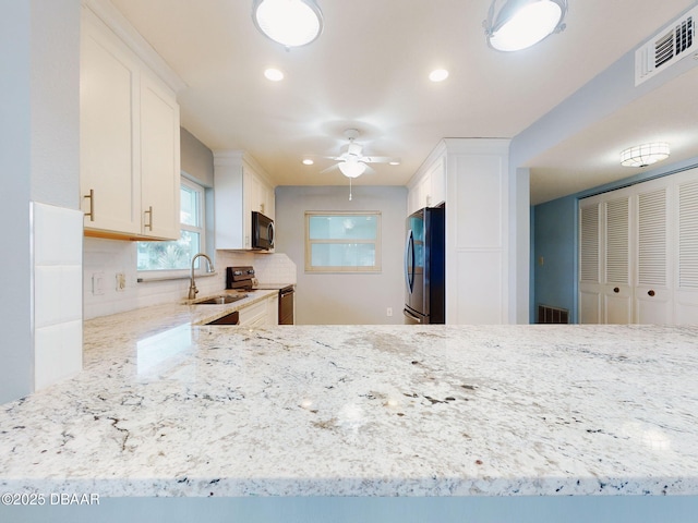 kitchen featuring sink, white cabinetry, tasteful backsplash, light stone counters, and black appliances