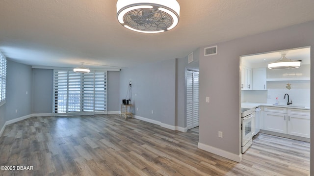 unfurnished living room with sink, a textured ceiling, and light hardwood / wood-style flooring