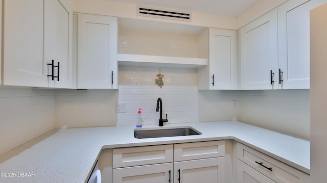 kitchen with tasteful backsplash, light stone countertops, sink, and white cabinets