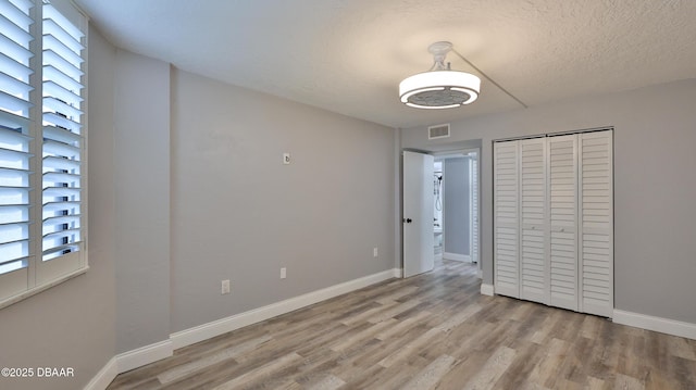 unfurnished bedroom featuring a textured ceiling, a closet, and light wood-type flooring