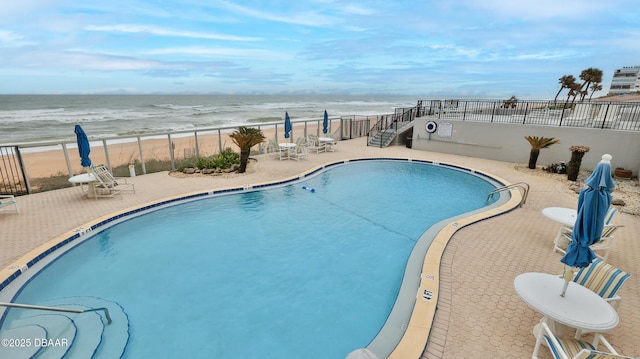 view of swimming pool with a water view, a beach view, and a patio area