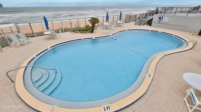 view of pool featuring a water view, a beach view, and a patio area