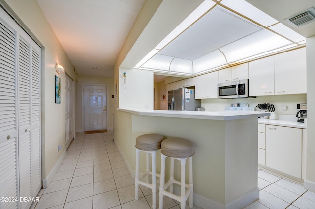 kitchen featuring a breakfast bar, kitchen peninsula, appliances with stainless steel finishes, light tile patterned floors, and white cabinets