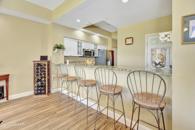 4670 Links Village Dr Unit B102, Ponce Inlet, FL 32127 - kitchen featuring stainless steel appliances, light wood finished floors, backsplash, a breakfast bar, and glass insert cabinets