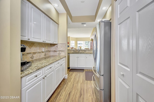 4670 Links Village Dr Unit B102, Ponce Inlet, FL 32127 - kitchen with freestanding refrigerator, white cabinetry, light wood-style floors, light stone counters, and tasteful backsplash