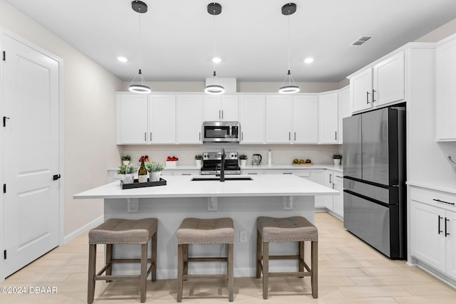 kitchen featuring appliances with stainless steel finishes, sink, an island with sink, and hanging light fixtures