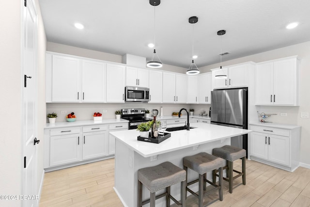 kitchen with white cabinetry, appliances with stainless steel finishes, hanging light fixtures, an island with sink, and light hardwood / wood-style flooring