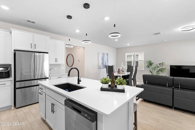 kitchen featuring stainless steel appliances, white cabinetry, sink, an island with sink, and pendant lighting