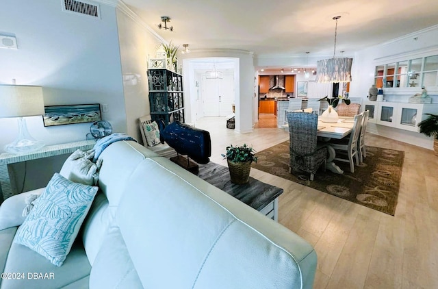 living room with a chandelier, light wood-type flooring, and ornamental molding