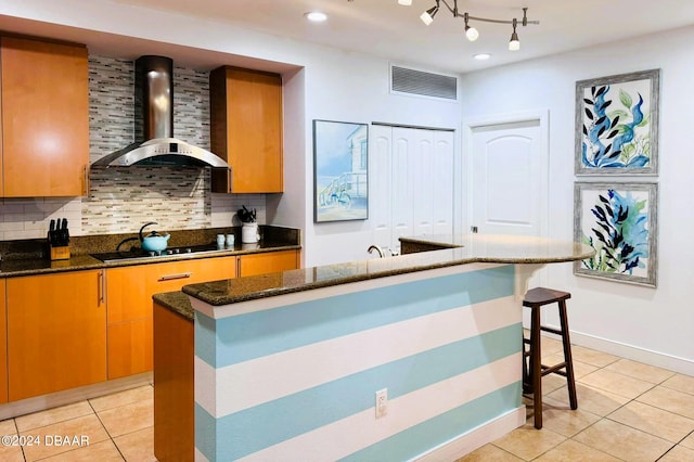 kitchen featuring black electric cooktop, a center island, wall chimney exhaust hood, light tile patterned floors, and dark stone countertops