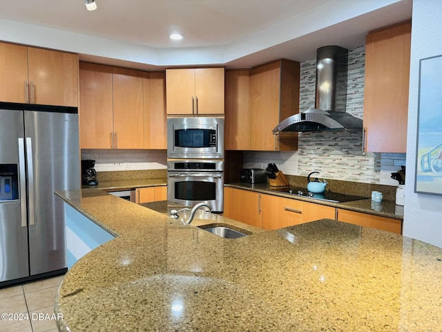 kitchen with stone countertops, wall chimney range hood, decorative backsplash, and appliances with stainless steel finishes