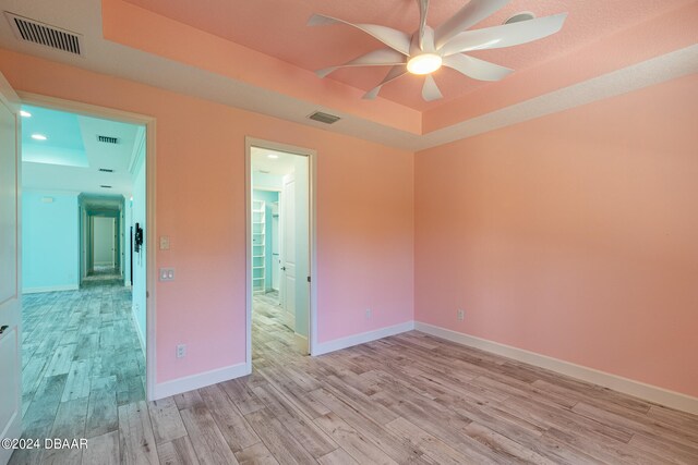 unfurnished room featuring light wood-type flooring, ceiling fan, and a raised ceiling