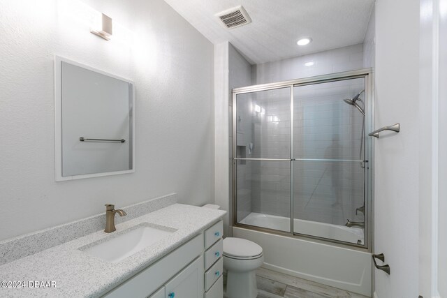 full bathroom featuring enclosed tub / shower combo, toilet, hardwood / wood-style floors, a textured ceiling, and vanity