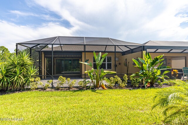 rear view of property with glass enclosure, a patio area, and a lawn