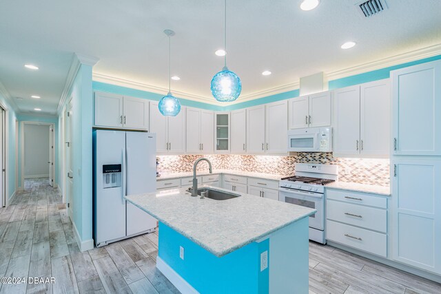 kitchen with hanging light fixtures, sink, a kitchen island with sink, ornamental molding, and white appliances