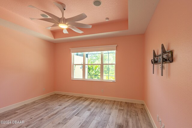 spare room with light hardwood / wood-style floors, ceiling fan, a textured ceiling, and a raised ceiling