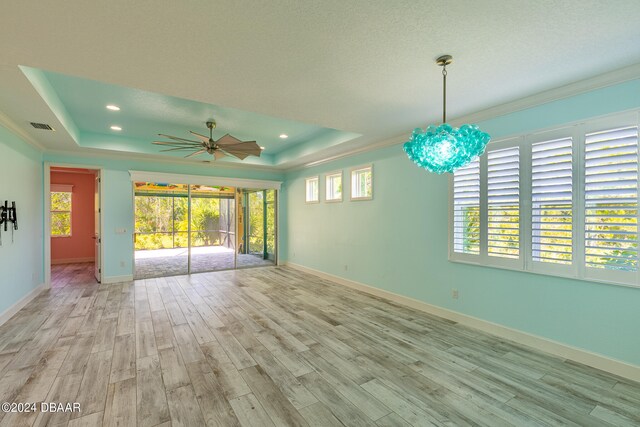 unfurnished room featuring ceiling fan with notable chandelier, a raised ceiling, light wood-type flooring, and ornamental molding