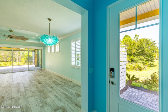 entryway with light hardwood / wood-style floors, ceiling fan with notable chandelier, and ornamental molding