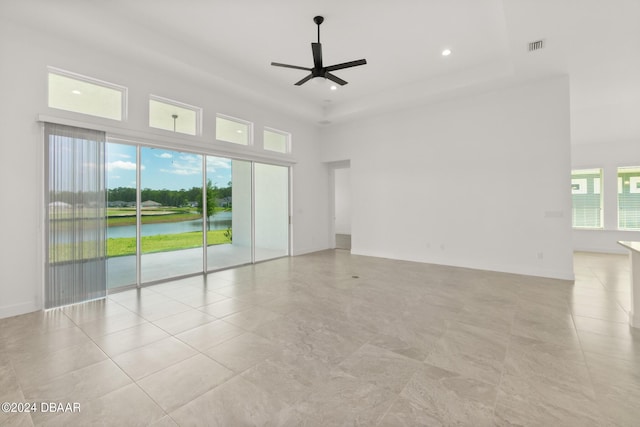 empty room featuring a water view, a towering ceiling, and ceiling fan